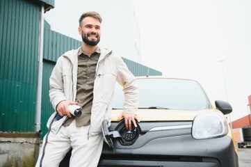 Man Holding Power Charging Cable For Electric Car In Outdoor Car Park. And he s going to connect the car to the charging station in the parking lot near the shopping center