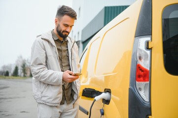 Casual man near electric car waiting for the finish of the battery charging process