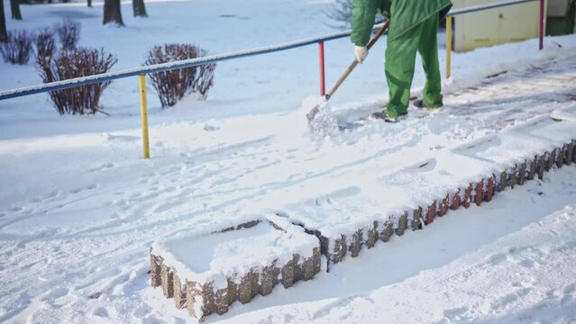 A worker in green work clothes clears snow from a private property in the city.