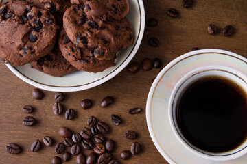 A cup of coffee with chocolate cookie on a dark wooden table. Spilled coffee beans. Top view.