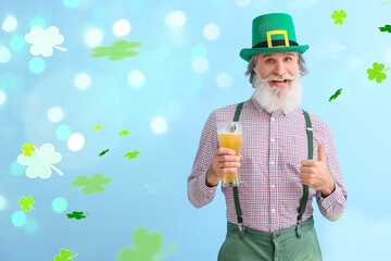Senior man with glass of beer showing thumb-up on light blue background. St. Patrick's Day...