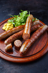 Gebratene Allgäuer Wagyu Rindsbratwurst mit scharfem Senf und Rucola serviert als close-up auf einem rustikalen Holz Schneidebrett