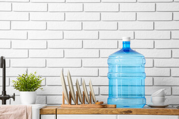 Bottle of clean water, plates and cups on kitchen counter near white brick wall