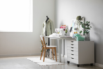 Tailor's workplace with sewing machine, pegboard and tablet computer in atelier