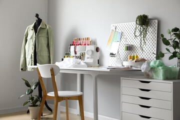 Tailor's workplace with sewing machine, pegboard and tablet computer in atelier