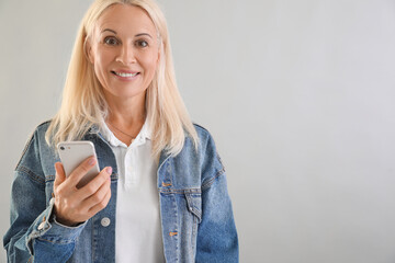 Fototapeta premium Mature blonde woman using mobile phone on light background