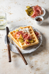 Cheese waffles with ham, cream cheese and cucumber with cutlery, text space on beige textured background. Delisious savory breakfast