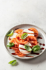 Caprese salad with tomatoes, basil, mozzarella, balsamic sauce and olive oil. Traditional Italian food on gray background, copy space