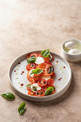 Caprese salad in modern linear feed with tomatoes, basil, mozzarella, pesto, balsamic sauce and olive oil. Traditional Italian food on beige background, copy space