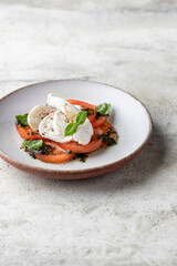 Caprese salad in modern feed with tomatoes, basil, mozzarella, pesto. Traditional Italian food on gray textured background isolated with text space, menu