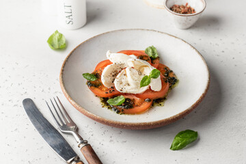 Caprese salad in modern feed with tomatoes, basil, mozzarella, pesto. Traditional Italian food with cutlery on white background, menu