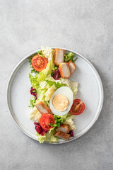 Caesar salad in modern linear feed with chicken, egg, tomatoes, lettuce and parmesan chips isolated on gray table, top view, flat lay, text space, menu