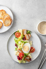 Caesar salad in modern linear feed with chicken, egg, tomatoes, lettuce and parmesan chips with cutlery on gray table, top view, flat lay, text space, menu