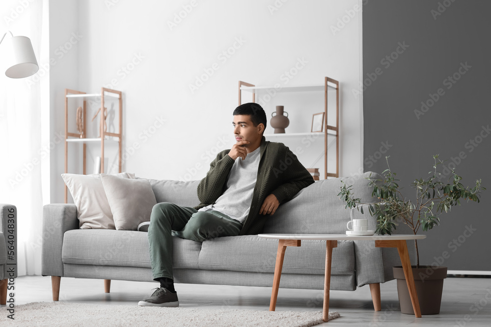 Poster Thoughtful young man sitting on sofa at home