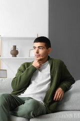 Thoughtful young man sitting on sofa at home