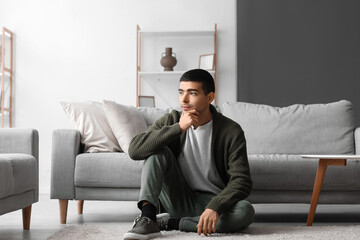 Thoughtful young man sitting on sofa at home