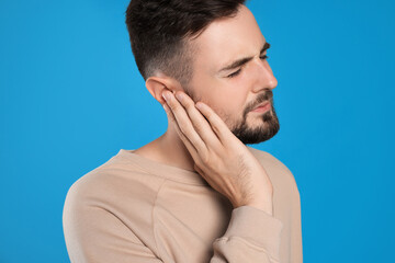 Fototapeta premium Young man suffering from ear pain on light blue background