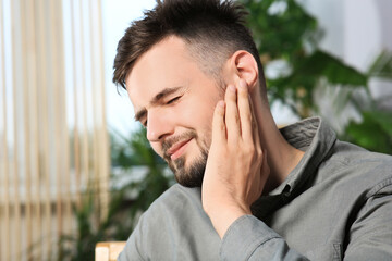 Young man suffering from ear pain at home