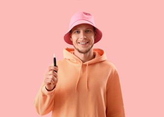 Young man in bucket hat with disposable electronic cigarette on pink background