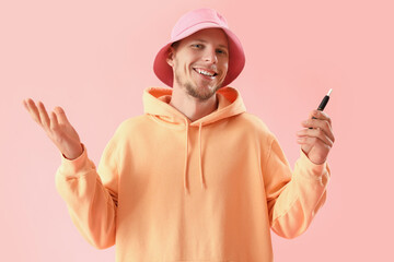Young man in bucket hat with disposable electronic cigarette on pink background