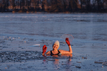 Winter swimming. Mature woman in frozen lake ice hole. Swimmers wellness and endorphin booster swim in cold water. Beautiful female body tempering Cold winter morning landscape. Biohacking routine