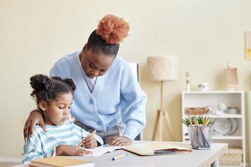 Caring mother helping little black girl studying at home