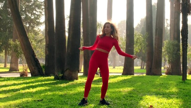 30s one woman with red tights and tops dancing at a public park on green grass with trees on the background