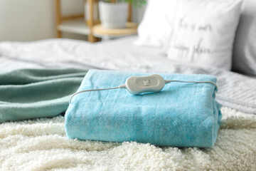 Folded electric heating pad with controller on bed in bedroom, closeup © Pixel-Shot