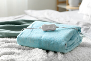 Folded electric heating pad with controller on bed in bedroom, closeup