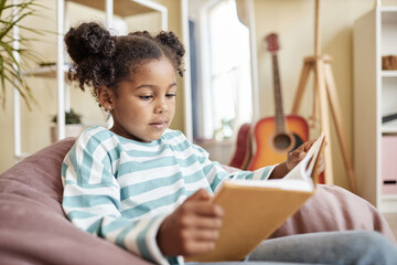 Fototapeta premium Little black girl reading book at home