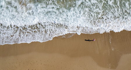 Aerial drone point of view unrecognised child play on sand  in a beach. Stormy waves idyllic beach in winter.