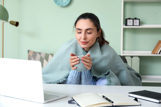 Frozen young woman with cup of tea working at home