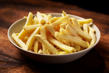 Frozen french fries on a plate on a wooden background. Semi-finished product from frozen potatoes.