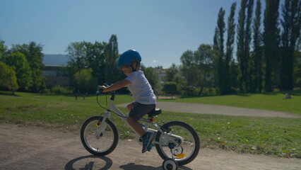Naklejka premium Child riding bike up a hill outside at park small boy rides bicycle