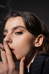 Fototapeta na wymiar portrait of stylish brunette woman smoking and looking at camera on black background.
