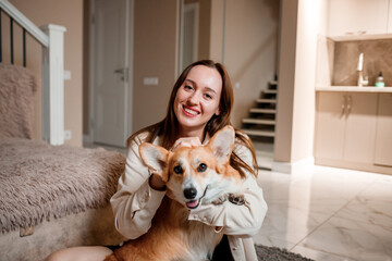 Attractive girl hug and play with corgi dog at home. Welsh Corgi Pembroke with his owner woman on the floor at living room