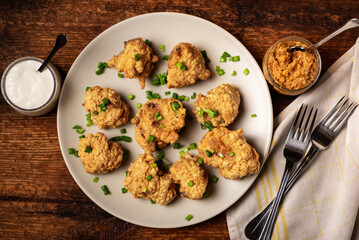 Cauliflower wings food. Pieces of cauliflower cooked in batter on a plate on a wooden background. Sprinkled with green onions.