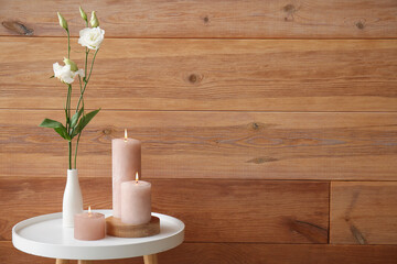 Burning candles and vase with eustoma flowers on end table near wooden wall