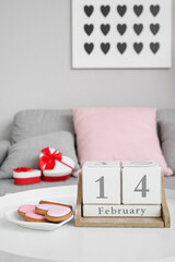 Calendar with date 14 FEBRUARY and cookies on table in living room, closeup