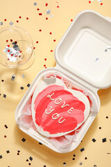 Plastic lunch box with heart-shaped bento cake and glass on beige background. Valentine's Day celebration