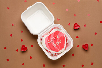 Plastic lunch box with heart-shaped bento cake and candles on brown background. Valentine's Day celebration