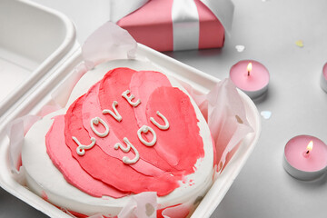 Plastic lunch box with heart-shaped bento cake and burning candles on grey background. Valentine's Day celebration