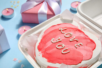 Plastic lunch box with heart-shaped bento cake, gift and burning candles on blue background, closeup. Valentine's Day celebration