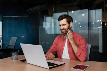 Office worker has a toothache, a sick businessman works inside the office with a laptop, a man has a toothache at the workplace.