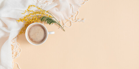 Hello spring concept. Spring trendy composition. White soft scarf, sprig of mimosa flowers and  cup...