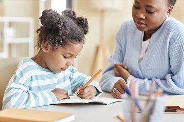 Side view cute black girl studying with tutor and writing in notebook