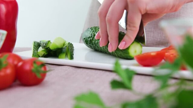 Healthy eating dieting concept. High angle view of female hands cutting cucumber in kitchen right side tomatoes sliced lettuce on left cucumbers white porcelain board gentle manicure young female hand