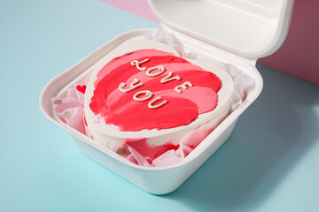 Lunch box with heart-shaped bento cake for Valentine's Day on table near pink wall, closeup