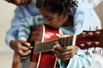 Candid cute black girl playing guitar with mother at home