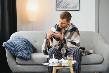 A sick man sits at home on a gray sofa with a blanket. Illness, protection, coronavirus, illness, flu